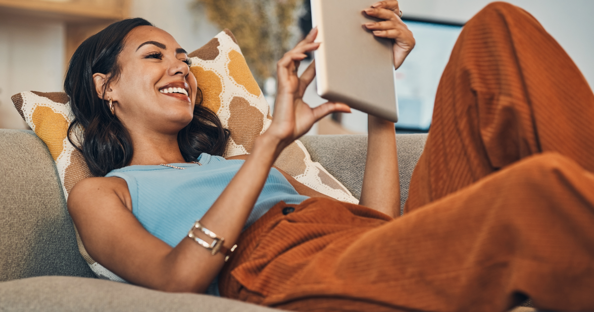 Vrouw ligt op de bank met een tablet in haar handen
